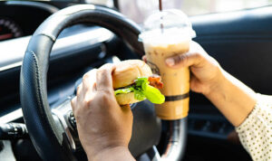 Asian woman driver hold and eat hamburger and cold coffee in car.